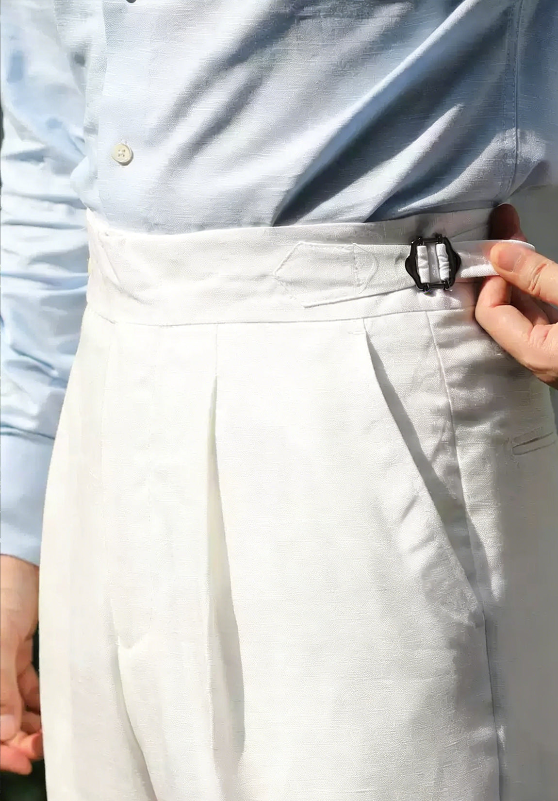 Men's white linen trousers with adjustable side tabs and double pleats.